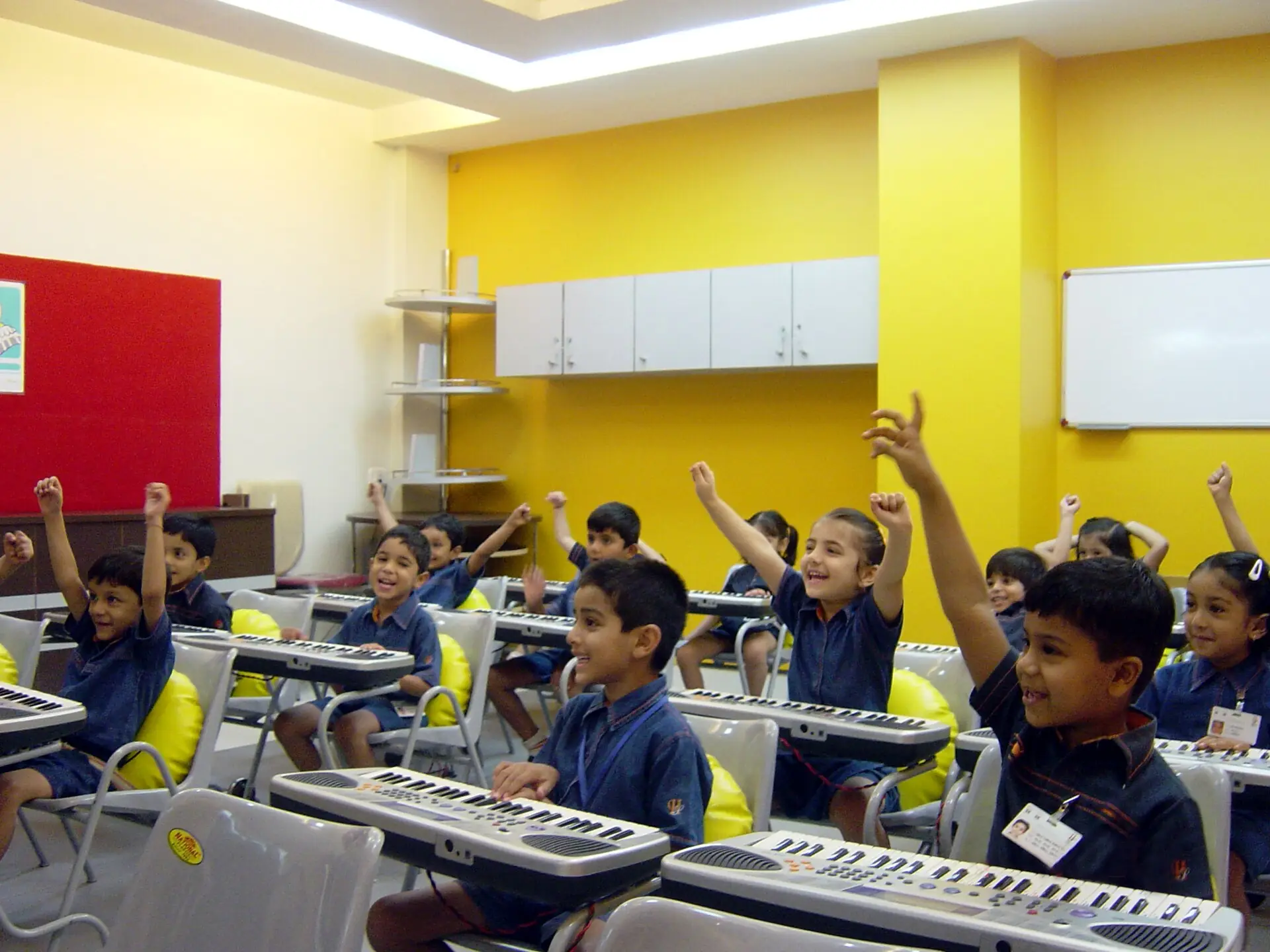 Young schoolchildren raising their hands eagerly in a brightly painted classroom